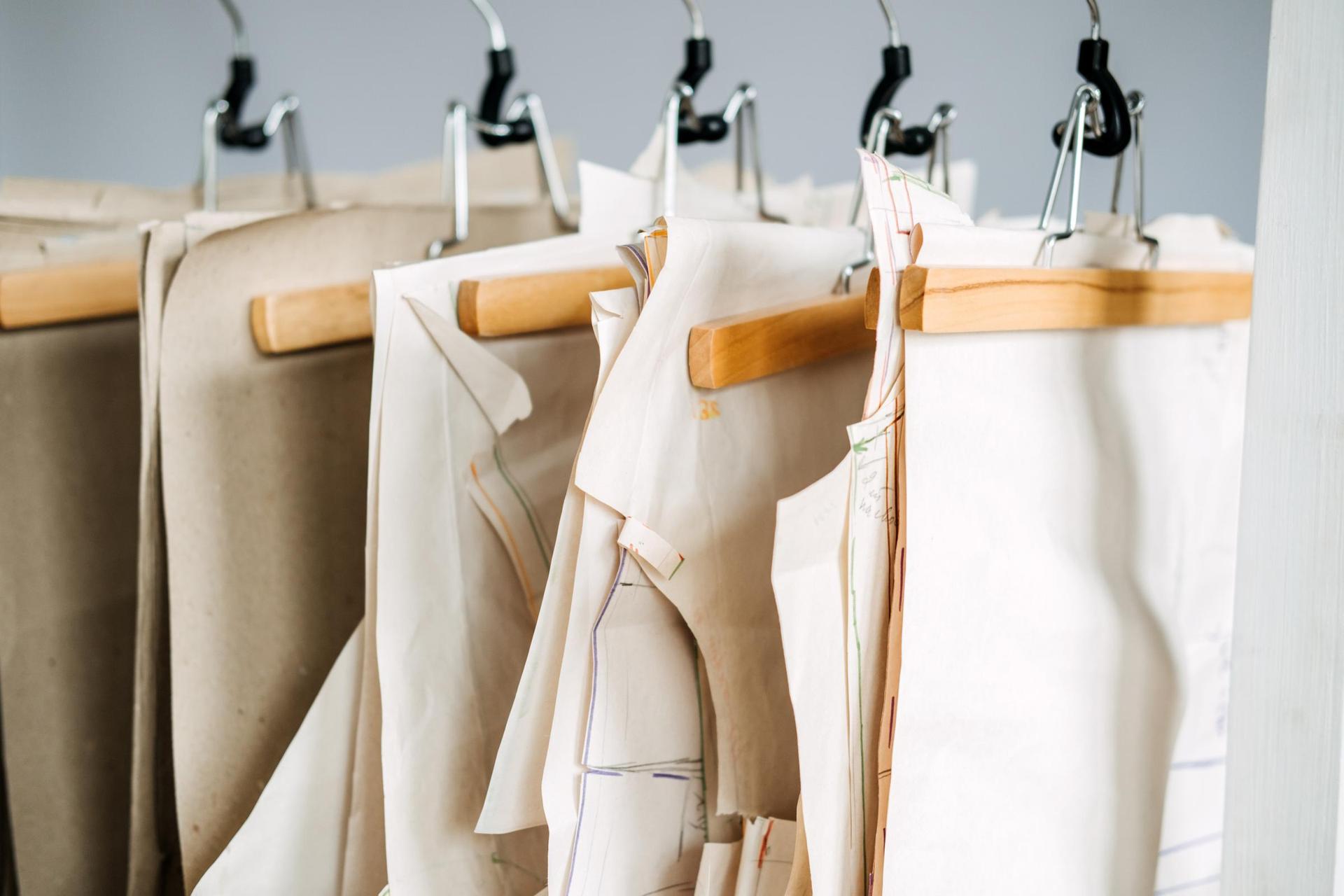 Paper sewing patterns for different clothes hanging on the rack in sewing factory.